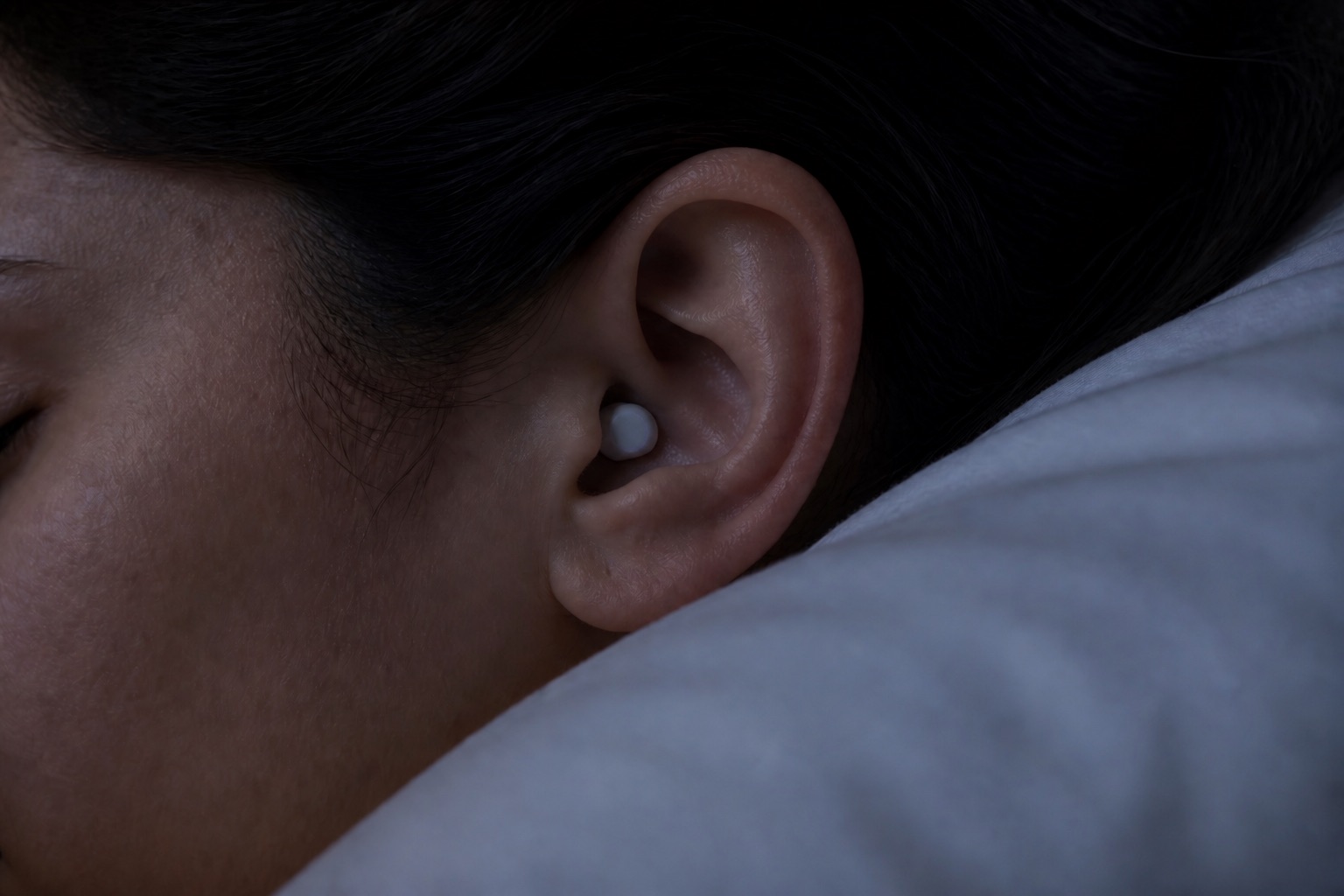 Side sleeper resting on a pillow with a low-profile DreamBud in their ear